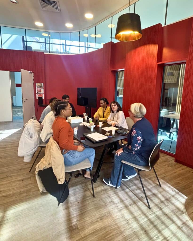 Photo de l'atelier "Coffee and tea time" à la Cité des Métiers CDG Alliance, animé par Fluency Formation. 7 professionnels sont assis autour d'une table, prennent un café et discutent en anglais.
